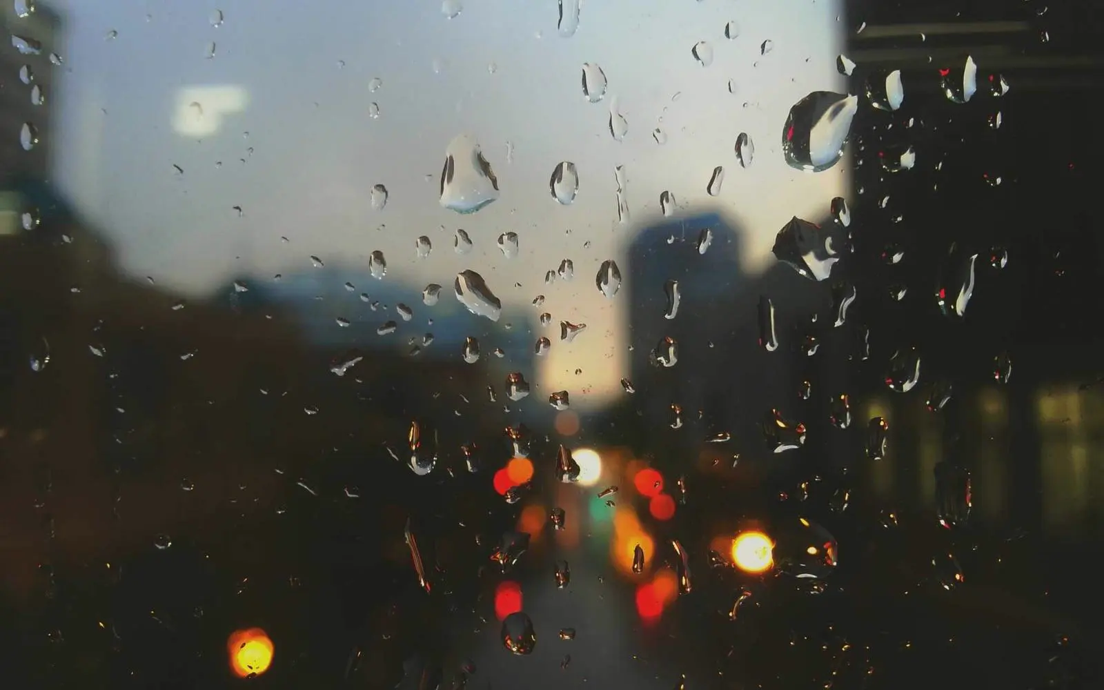 Rain on a window at night, with blurred traffic lights beyond.